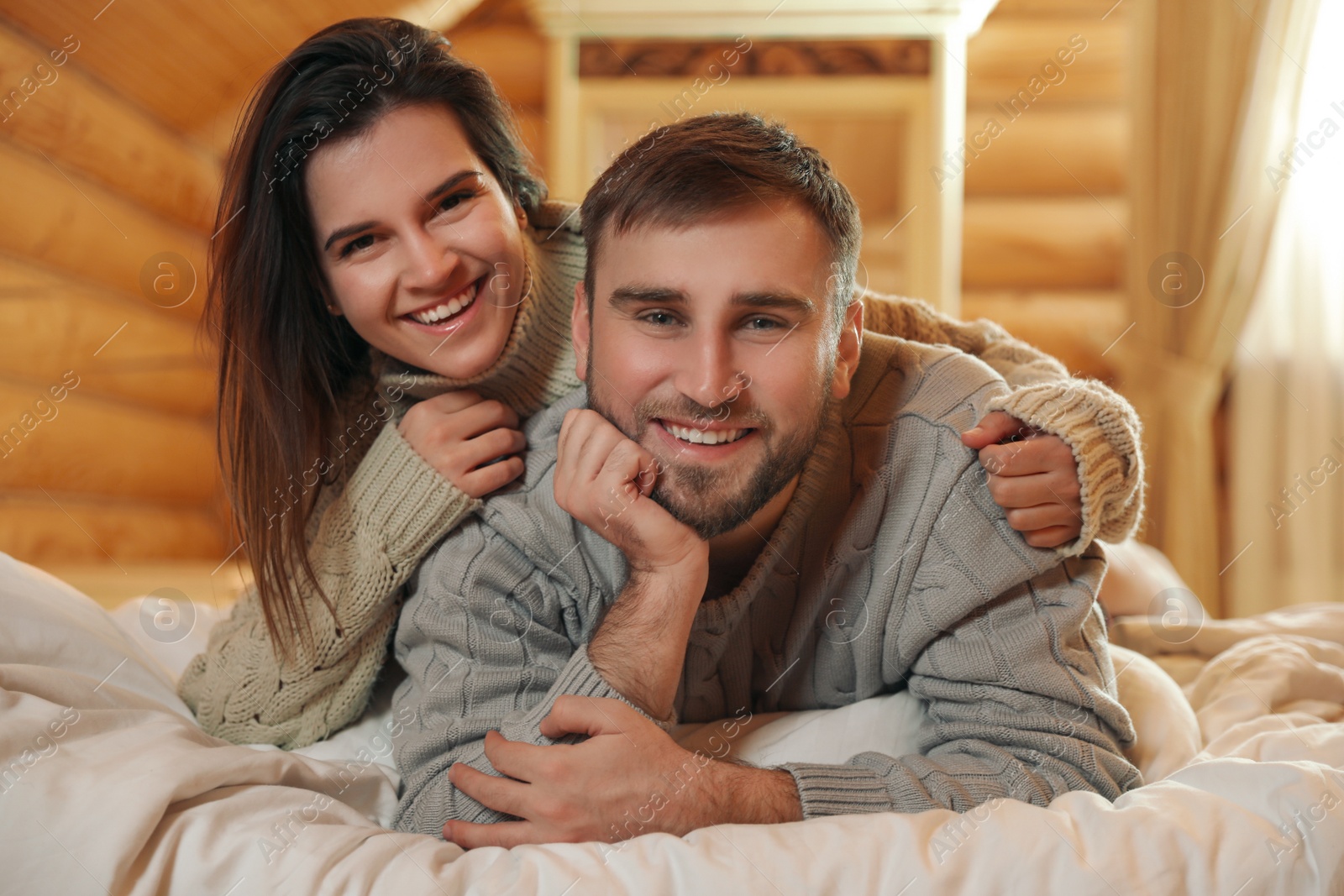 Photo of Young couple wearing warm sweaters on bed at home