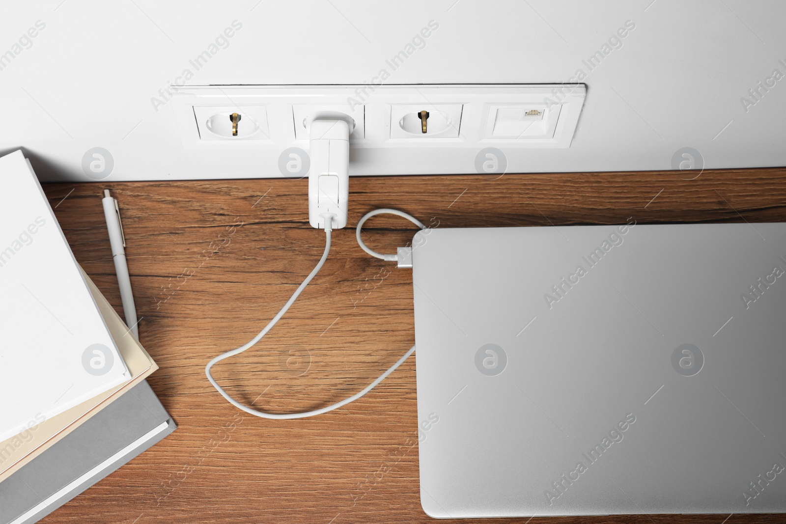 Photo of Modern laptop charging on wooden table, above view