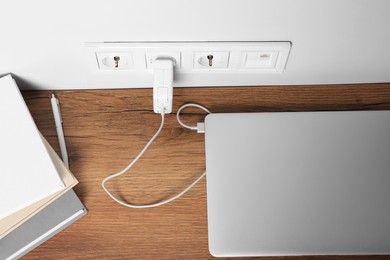 Photo of Modern laptop charging on wooden table, above view