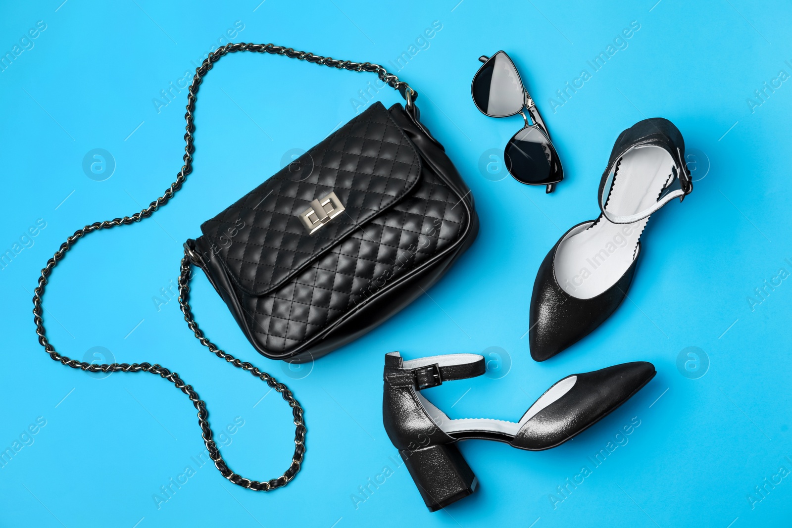 Photo of Stylish black female shoes, bag and glasses on light blue background, flat lay