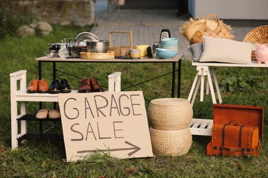 Sign Garage sale written on cardboard near tables with different stuff in yard