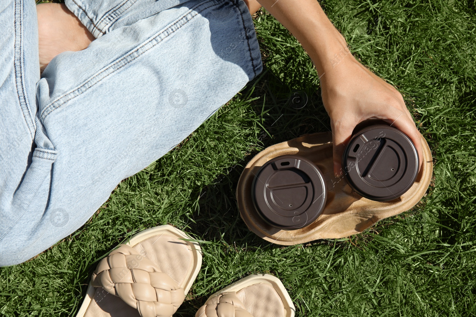 Photo of Woman holding takeaway cardboard coffee cups with plastic lids on green grass, top view