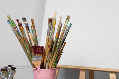 Photo of Easel with blank canvas and different art supplies near white wall. Space for text