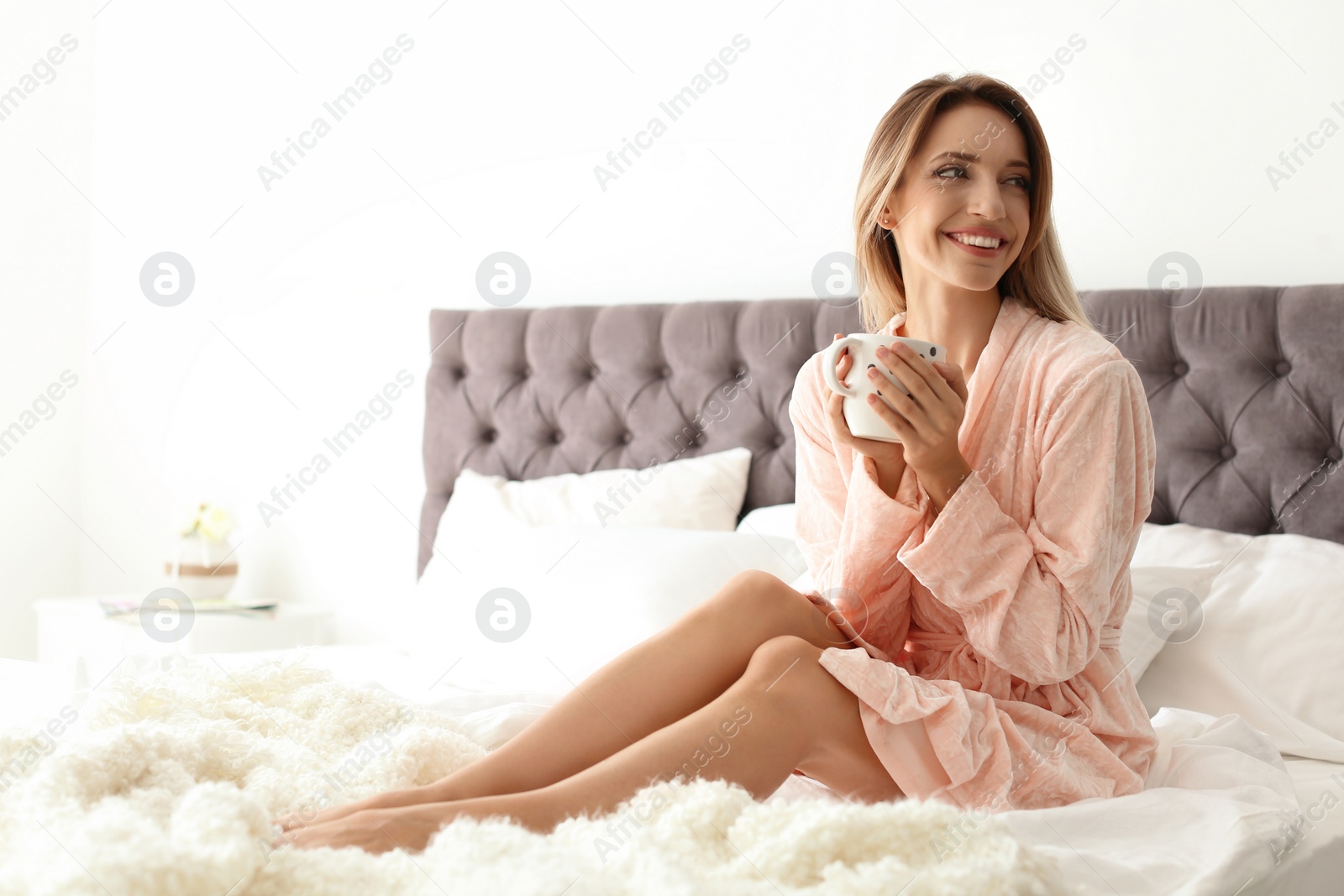 Photo of Beautiful young woman with cup of coffee sitting in bed at home. Lazy morning