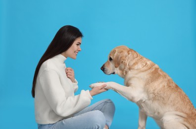 Photo of Cute Labrador Retriever giving paw to happy woman on light blue background