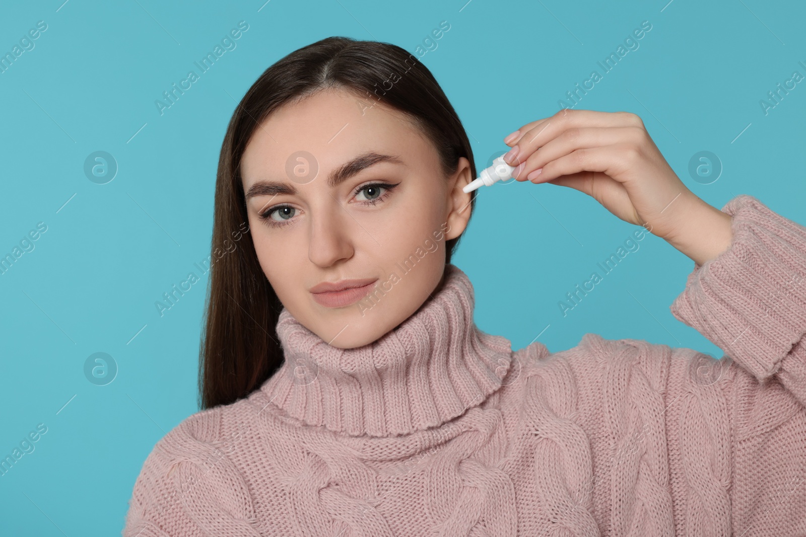 Photo of Young woman using ear drops on light blue background