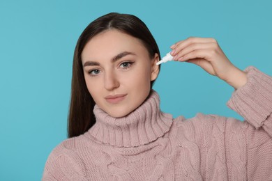 Young woman using ear drops on light blue background