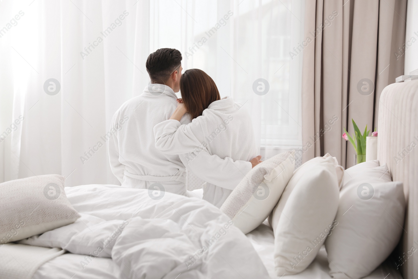 Photo of Happy couple in bathrobes sitting on bed at home