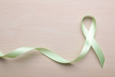 Photo of World Mental Health Day. Green ribbon on wooden background, top view with space for text