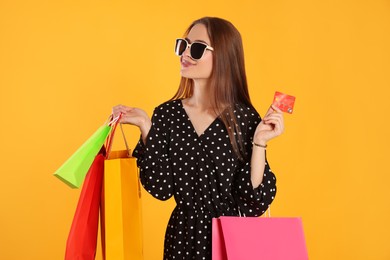 Photo of Happy young woman with shopping bags and credit card on yellow background. Big sale