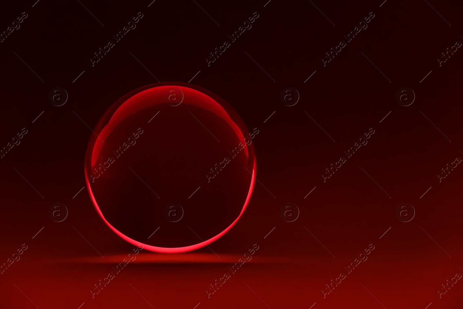 Photo of Transparent glass ball on dark red background. Space for text