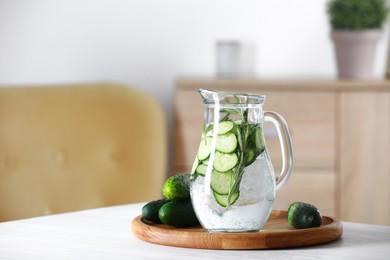 Refreshing cucumber water with rosemary in jug and vegetables on white table. Space for text