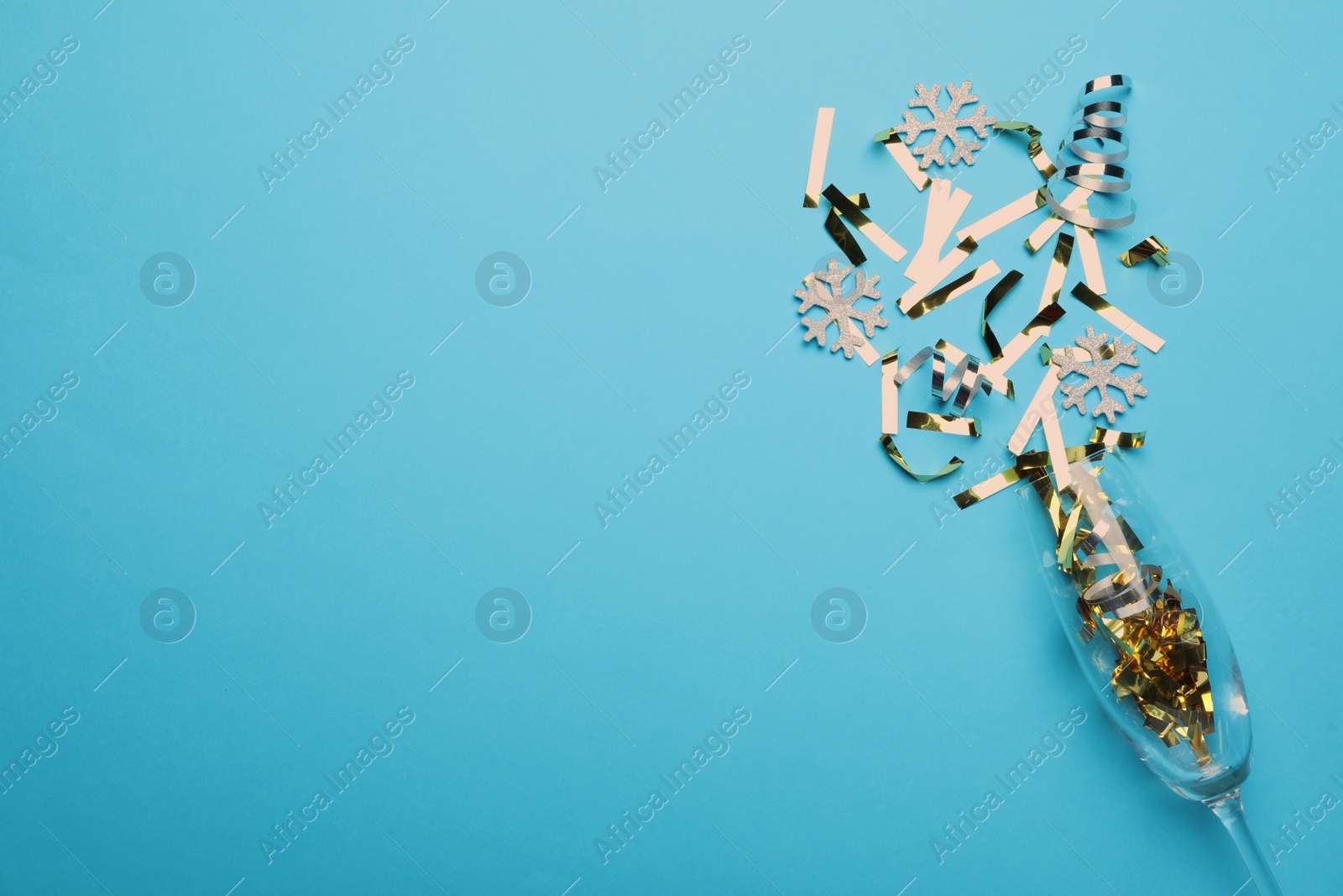 Photo of Glass and shiny confetti on light blue background, flat lay. Space for text