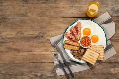 Plate of fried eggs, sausages, mushrooms, beans, bacon and toasts on wooden table, flat lay with space for text. Traditional English breakfast