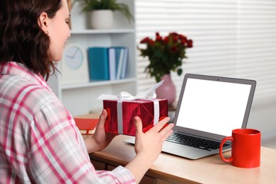 Valentine's day celebration in long distance relationship. Woman holding gift box while having video chat with her boyfriend via laptop indoors, closeup