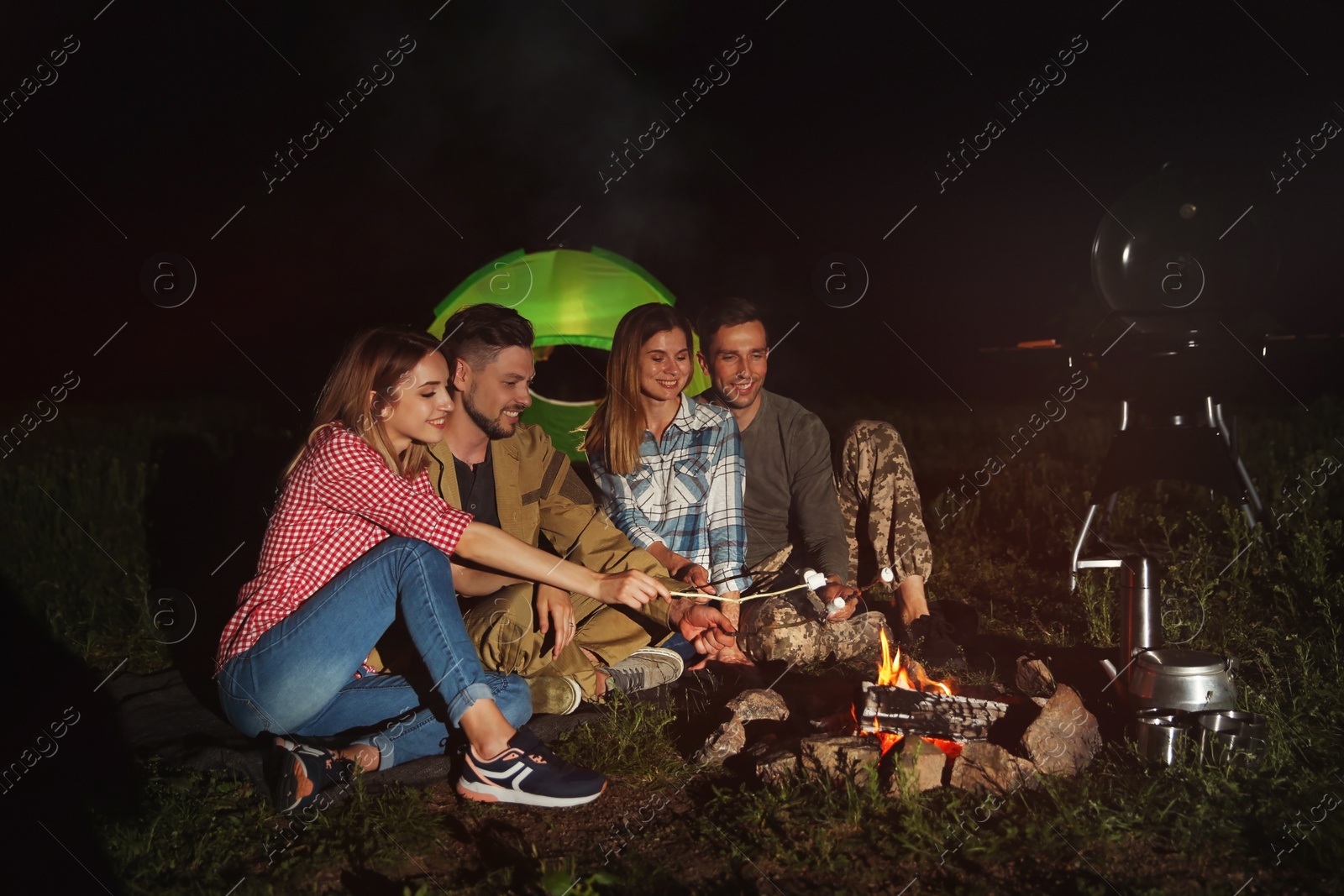 Photo of Friends frying marshmallows on bonfire at night. Camping season