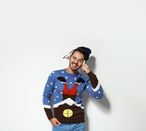 Young man in Christmas sweater and hat on white background