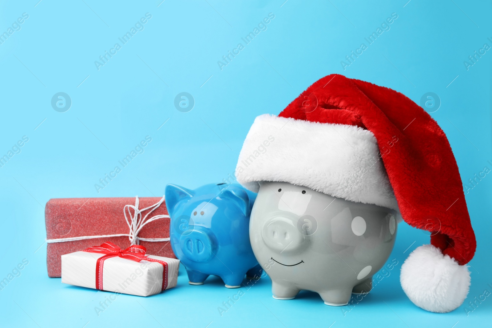 Photo of Piggy banks with Santa hat and gift boxes on light blue background