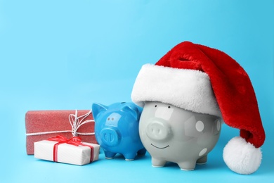 Photo of Piggy banks with Santa hat and gift boxes on light blue background