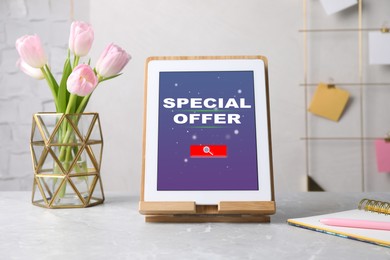 Image of Modern tablet with phrase Special Offer, stationery and flowers on grey marble table