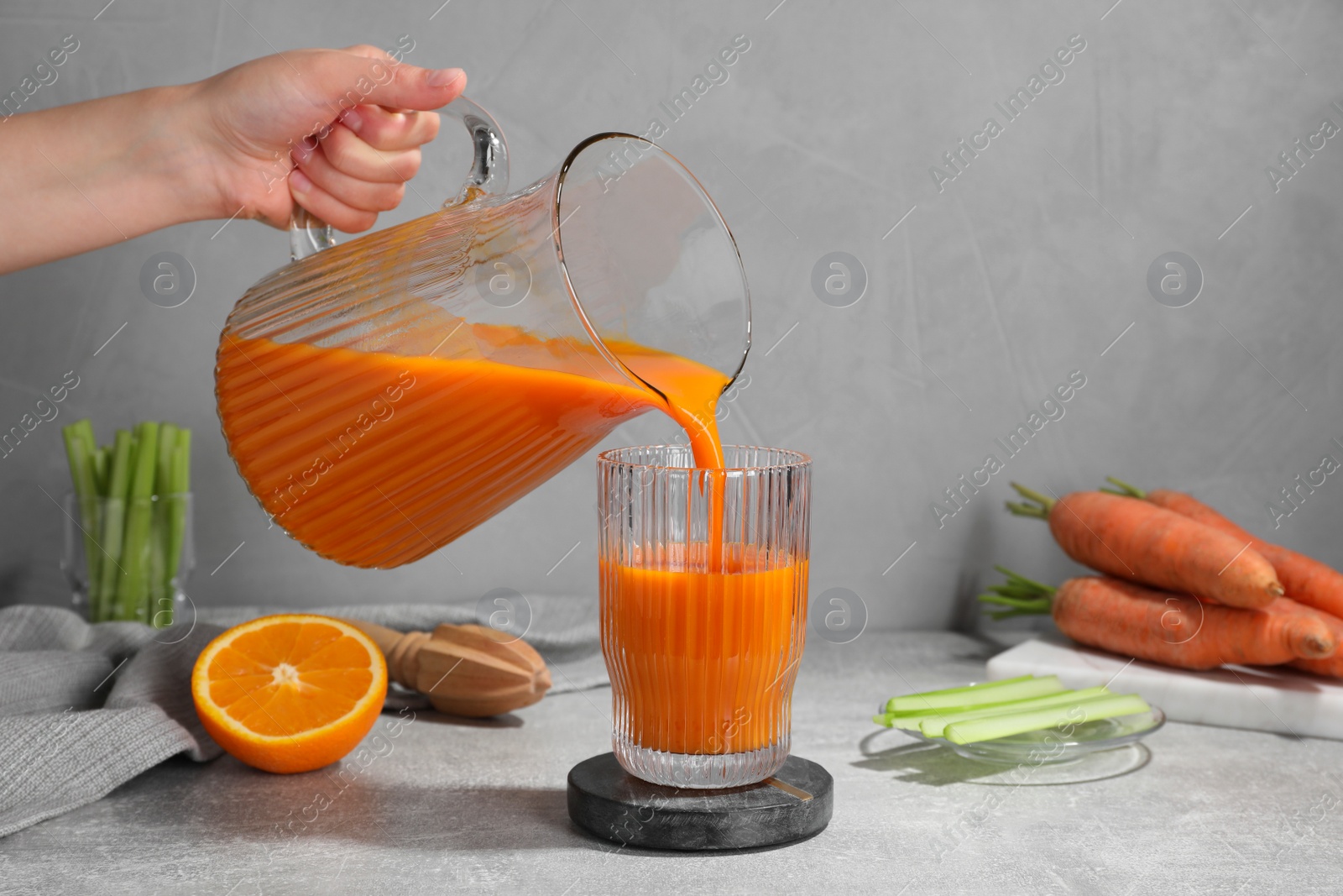 Photo of Woman pouring carrot juice from jug into glass at light grey table, closeup