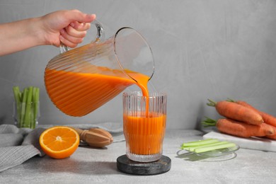 Woman pouring carrot juice from jug into glass at light grey table, closeup