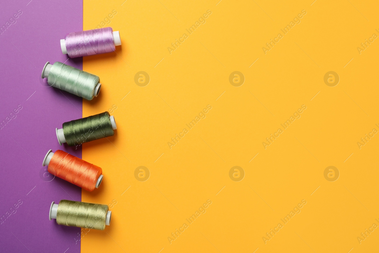 Photo of Set of different sewing threads on color background, flat lay. Space for text
