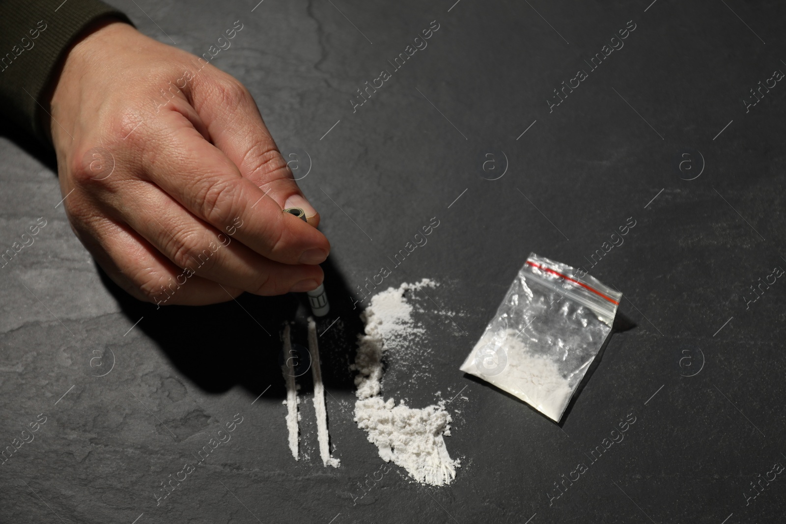 Photo of Addicted man with hard drug and rolled dollar banknote preparing for consumption at grey textured table, closeup