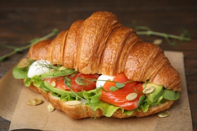 Photo of Tasty croissant with salmon, avocado, mozzarella and lettuce on wooden table, closeup