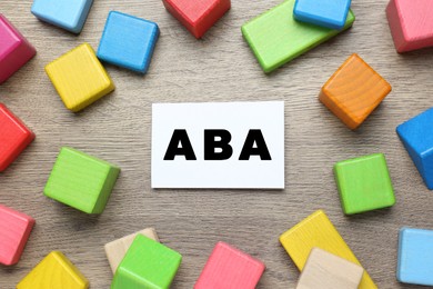 Photo of Colorful building blocks and card with abbreviation ABA on wooden table, flat lay