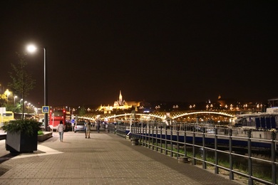 Photo of BUDAPEST, HUNGARY - APRIL 27, 2019: Beautiful night cityscape with people walking embankment along Danube river