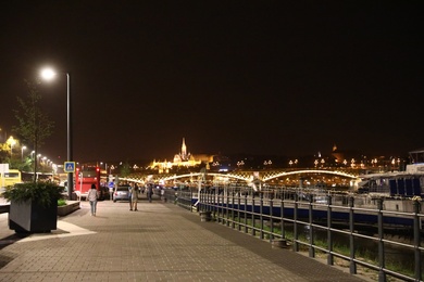 BUDAPEST, HUNGARY - APRIL 27, 2019: Beautiful night cityscape with people walking embankment along Danube river