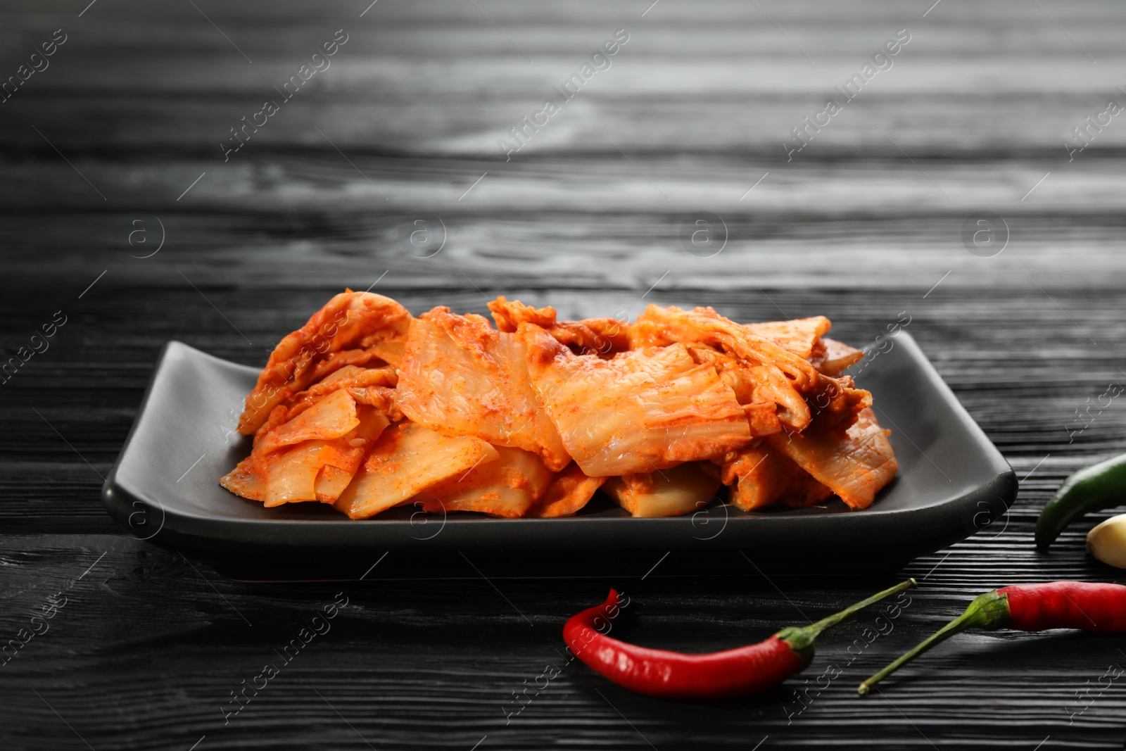 Photo of Delicious kimchi with Chinese cabbage and red chili peppers on black wooden table