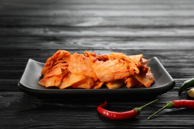 Photo of Delicious kimchi with Chinese cabbage and red chili peppers on black wooden table