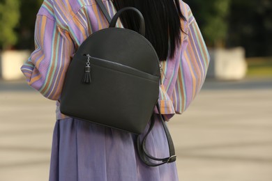 Photo of Young woman with stylish backpack on city street, closeup. Back view