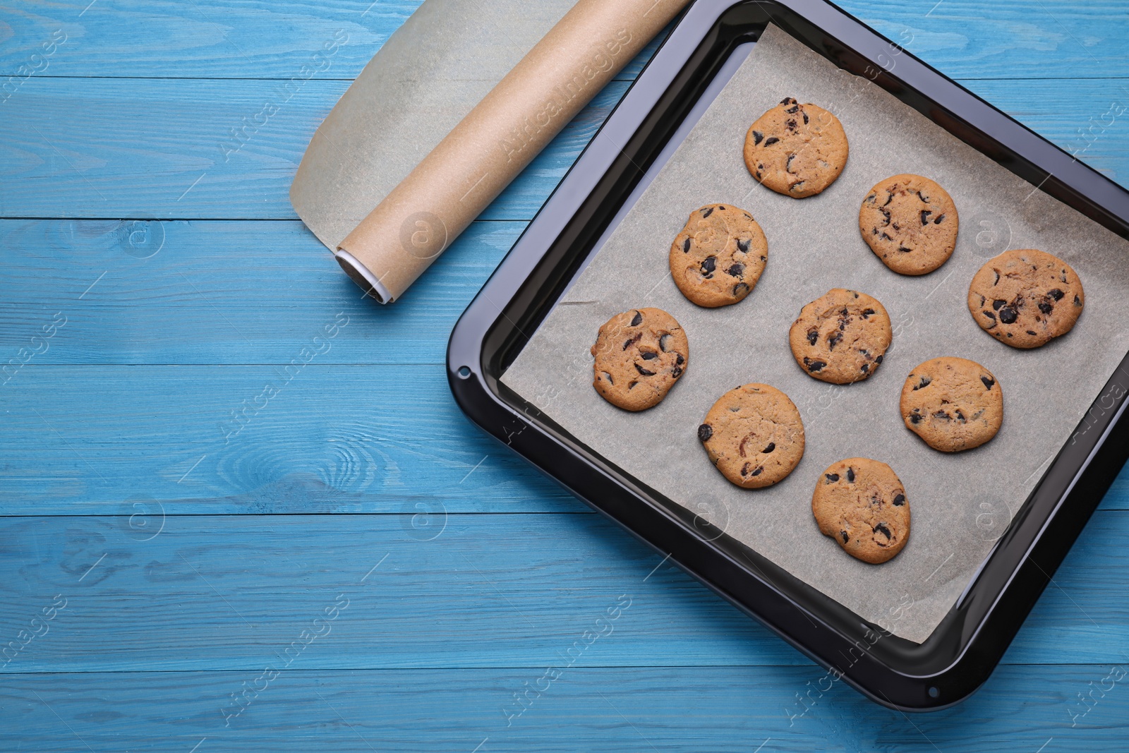 Photo of Parchment paper and baking pan with tasty cookies on light blue wooden table, flat lay. Space for text