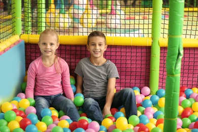 Cute little children playing in ball pit at indoor amusement park