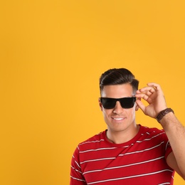 Handsome man wearing sunglasses on yellow background. Space for text