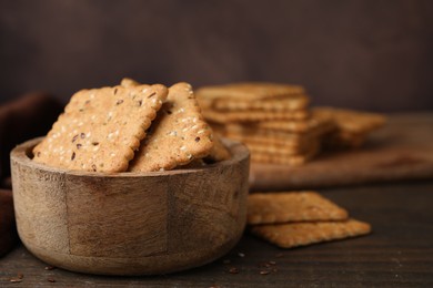Photo of Cereal crackers with flax and sesame seeds in bowl on wooden table, closeup. Space for text