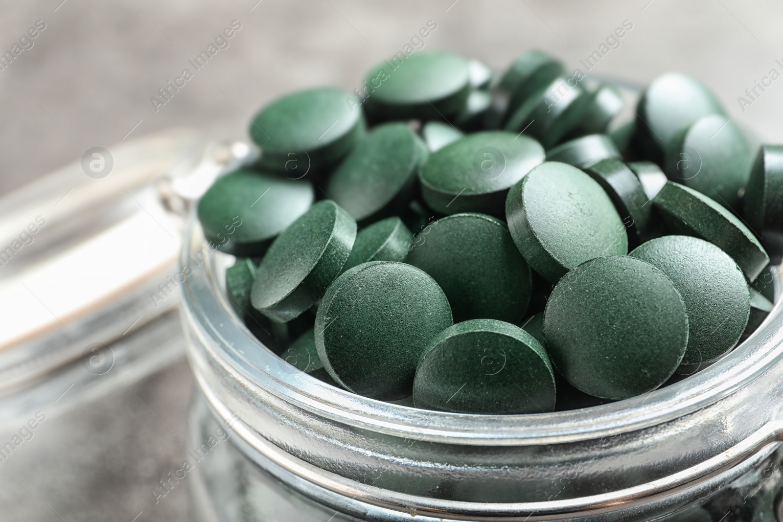 Photo of Glass jar with green spirulina pills on grey table, closeup