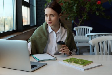 Photo of Young female student with laptop and coffee studying at table in cafe