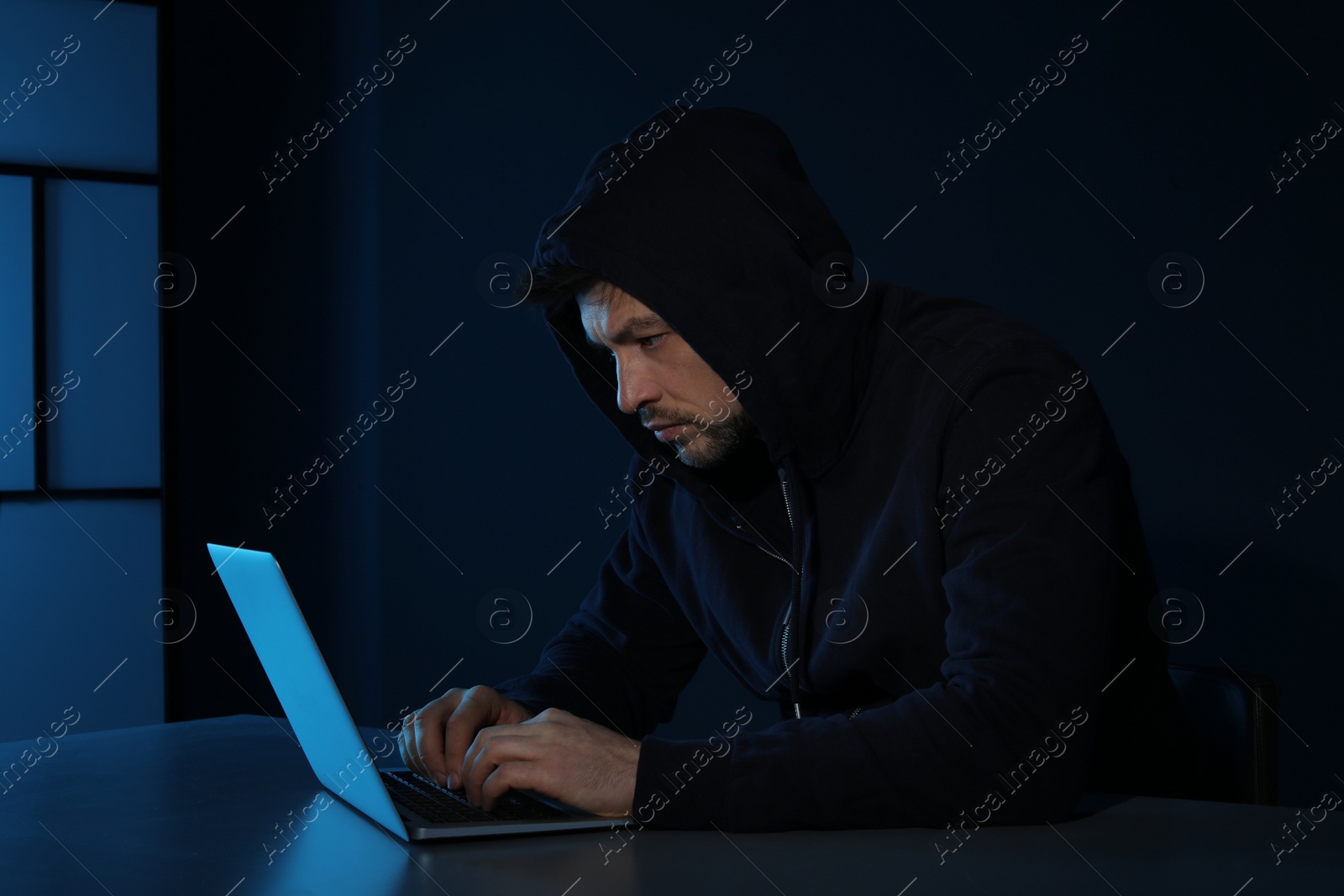 Photo of Man using laptop in dark room. Criminal offence