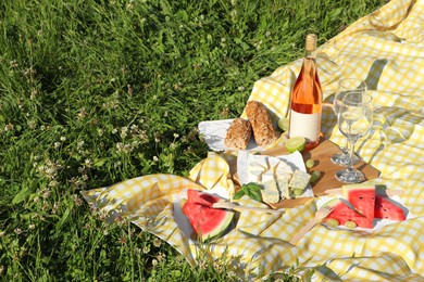 Photo of Picnic blanket with delicious food and wine on green grass outdoors, space for text