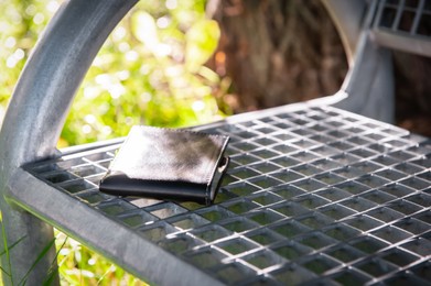 Black wallet on metal bench outdoors. Lost and found