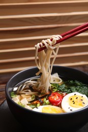 Photo of Eating delicious vegetarian ramen with chopsticks at table, closeup. Noodle soup