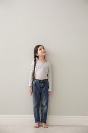 Photo of Little girl measuring her height near light grey wall indoors