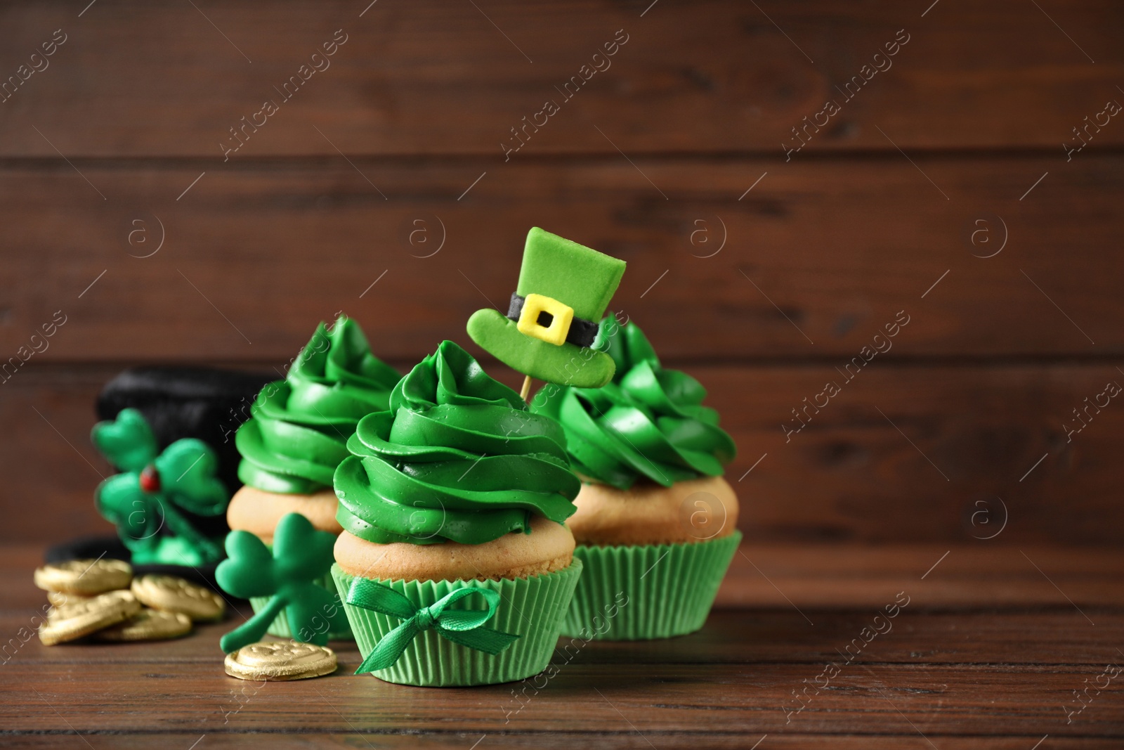 Photo of Decorated cupcakes and coins on wooden table, space for text. St. Patrick's Day celebration