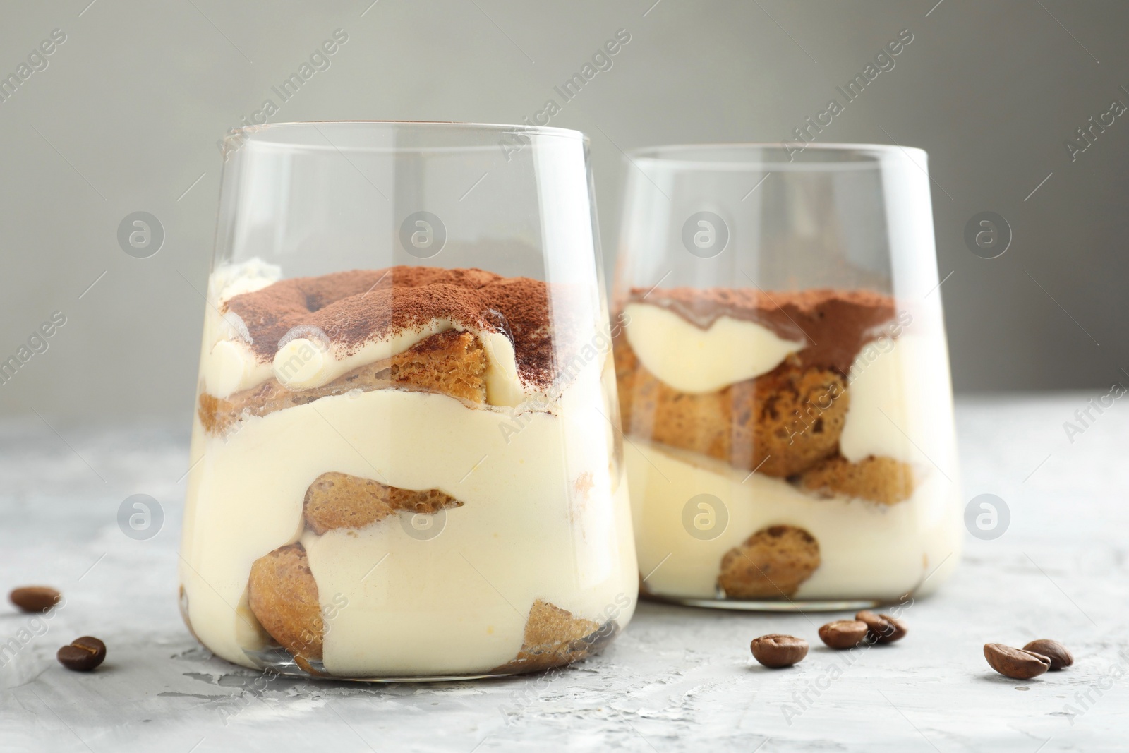 Photo of Delicious tiramisu in glasses and coffee beans on grey textured table, closeup