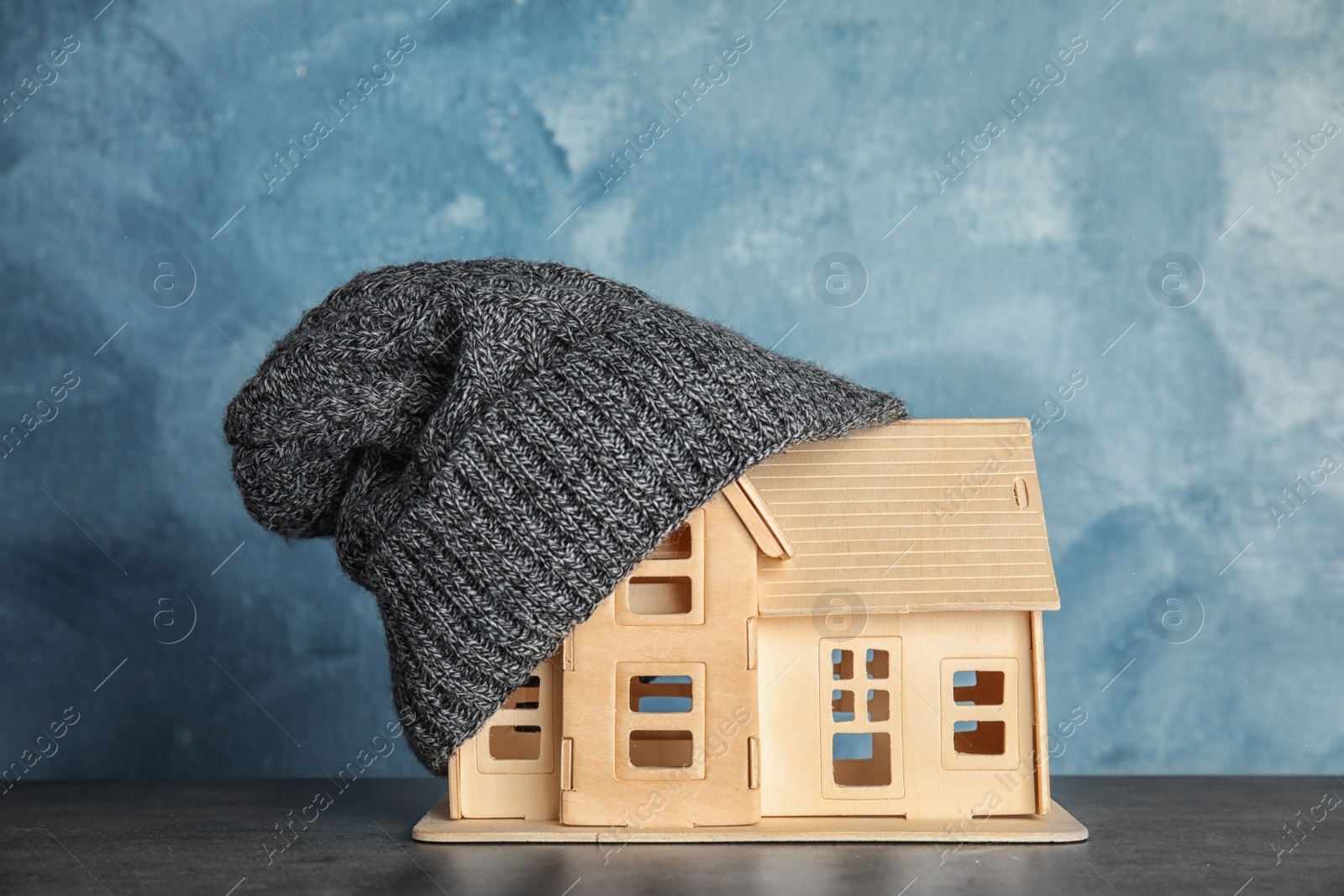 Photo of House model with knitted hat on table against color background. Heating concept