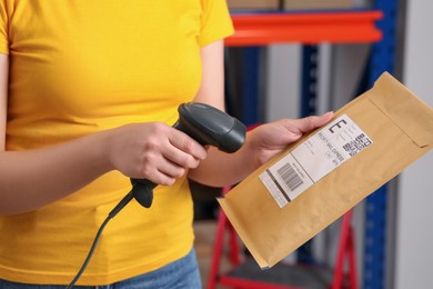 Photo of Post office worker with scanner reading parcel barcode indoors, closeup